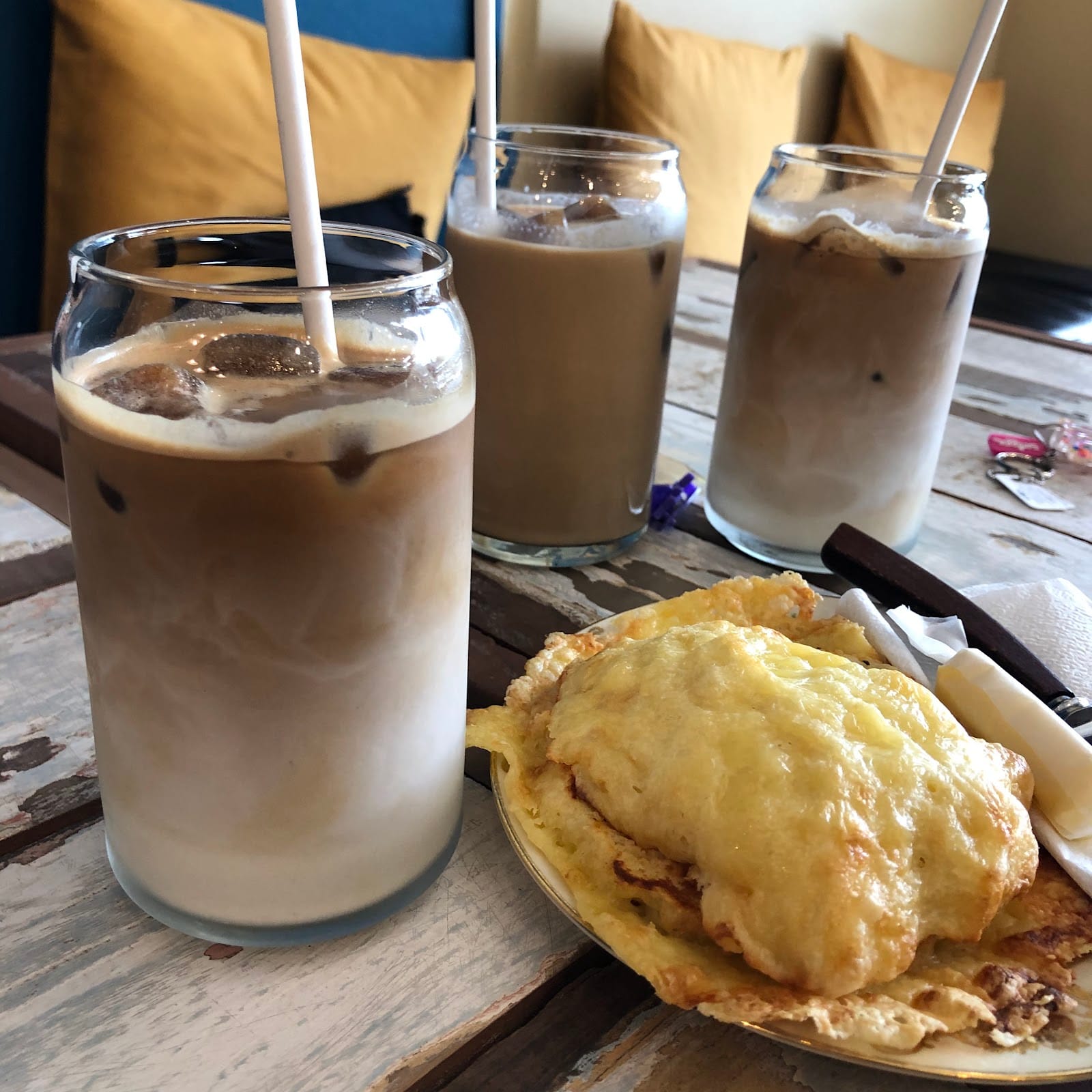 Three iced coffees and a cheese-topped bake on a wooden table.