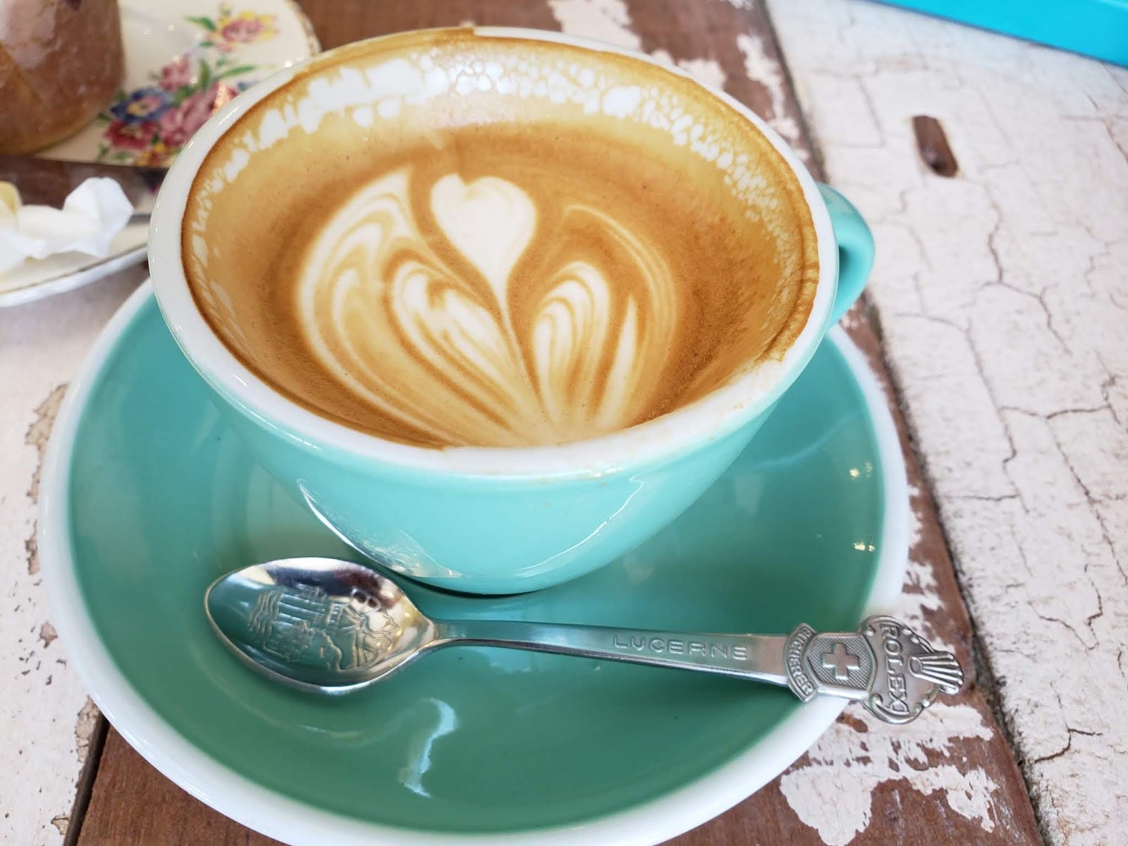 Latte art in a turquoise cup and saucer on a worn wooden table.