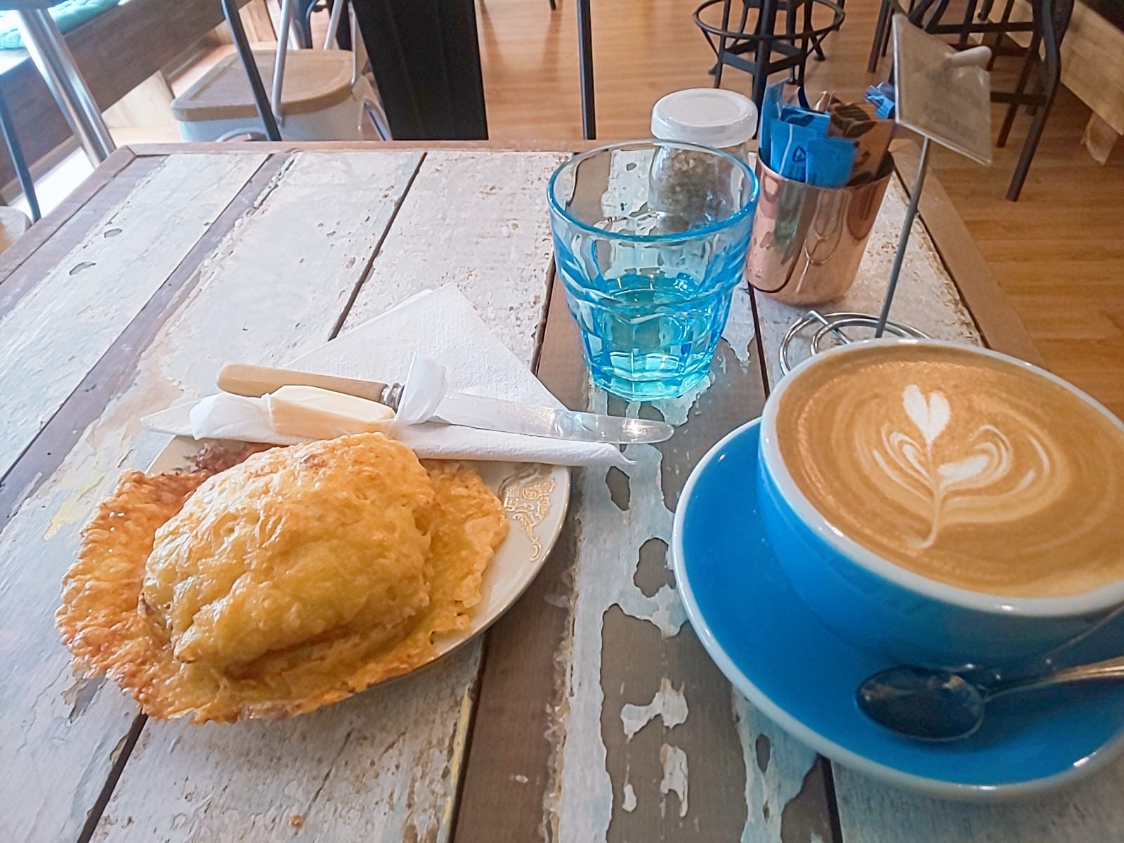 Latte in a blue cup beside a baked treat and a glass of water.