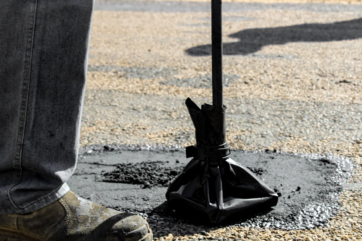 Worker applying a patch to a damaged asphalt surface