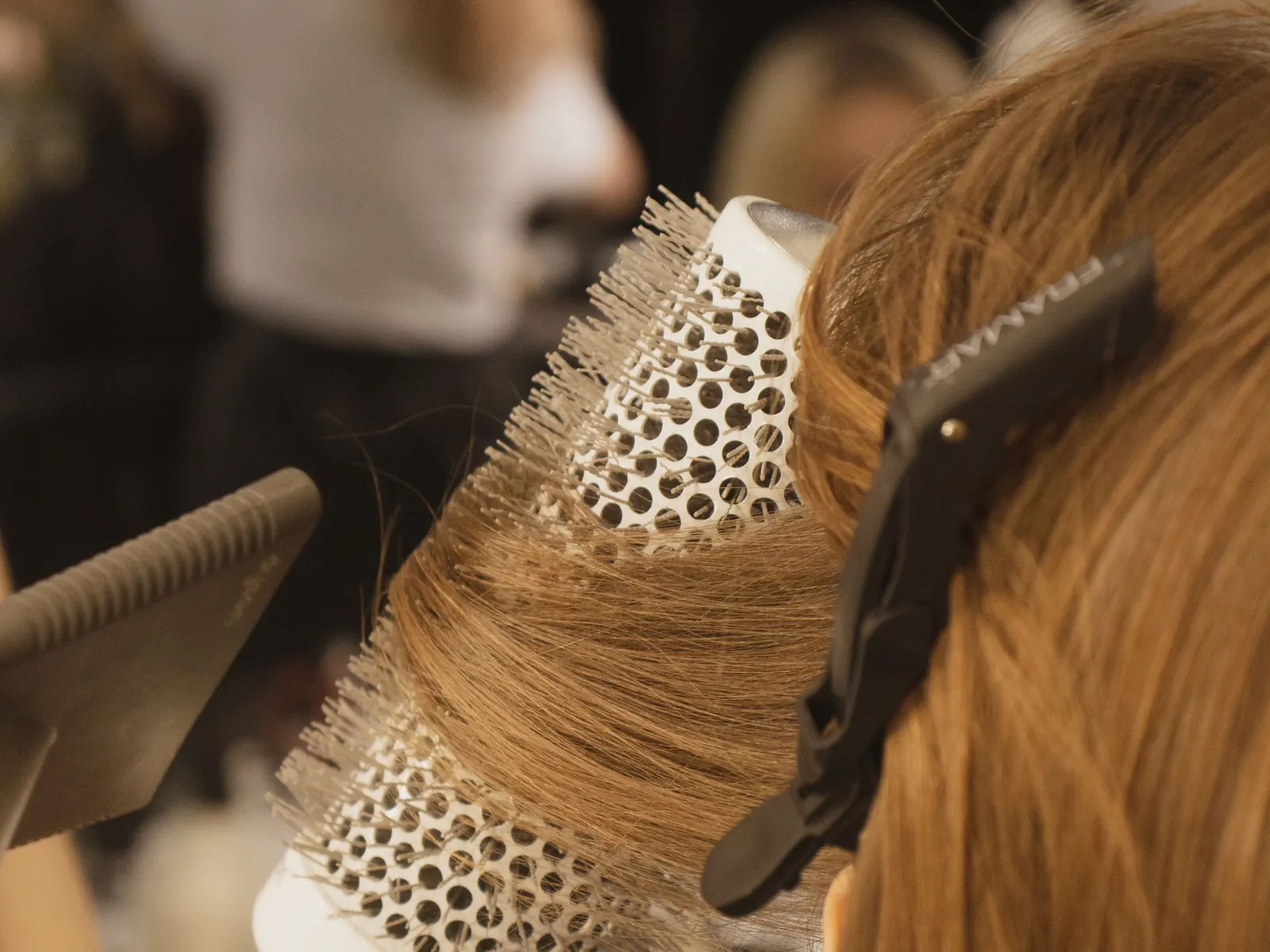 A round brush lifting a section of long hair during a blow-dry.