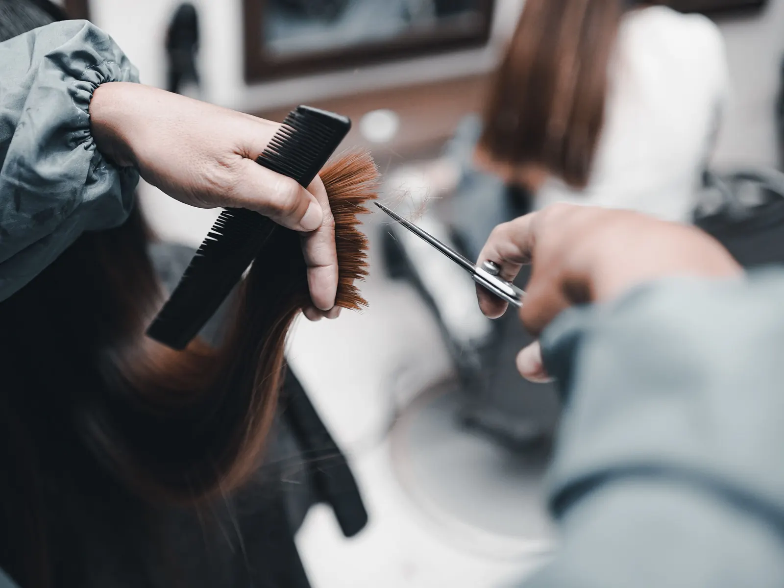 A stylist holding a comb and scissors while trimming the ends of long hair.