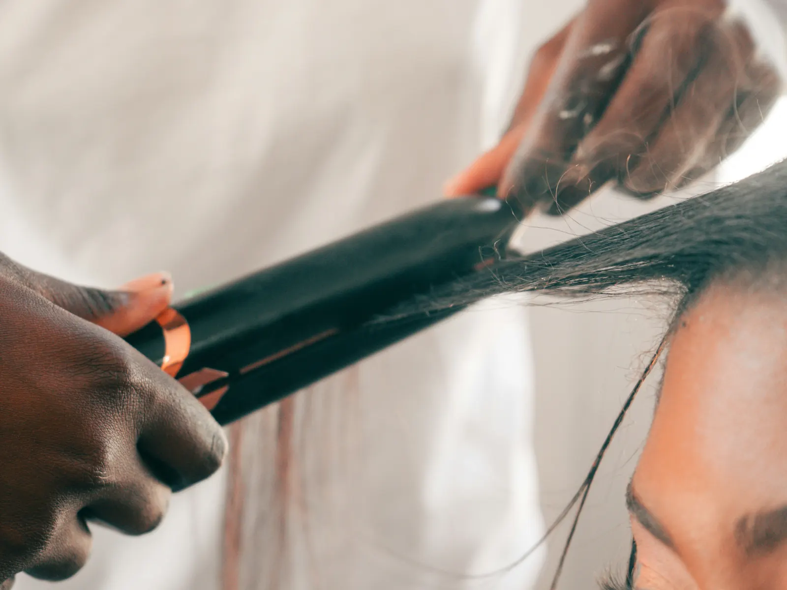 Hands guiding a flat iron down a section of dark hair.
