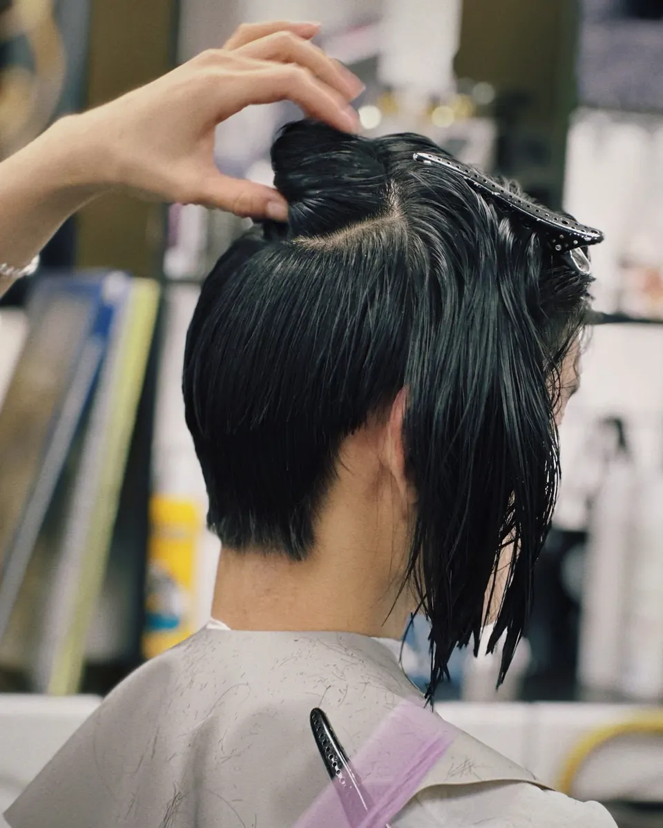 A stylist lifting a section of a short black cut.