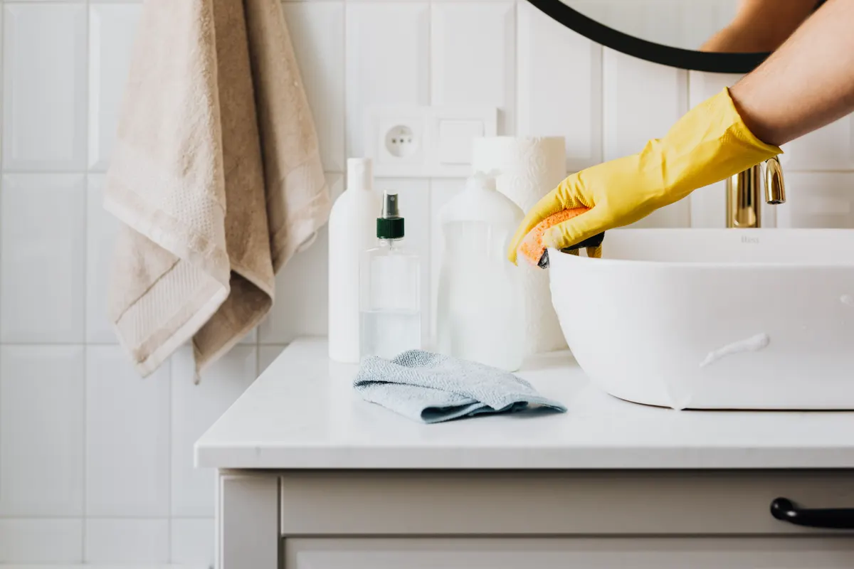 A gloved hand wiping a bathroom basin.