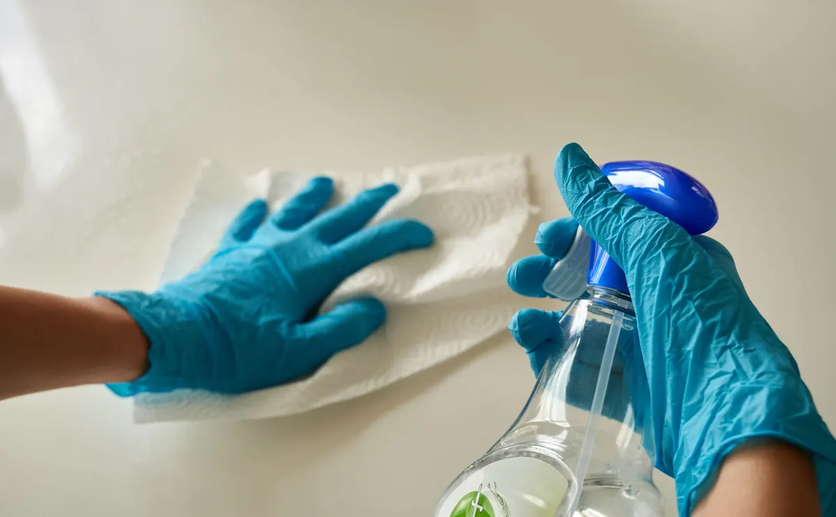 Gloved hands spraying and wiping a surface.