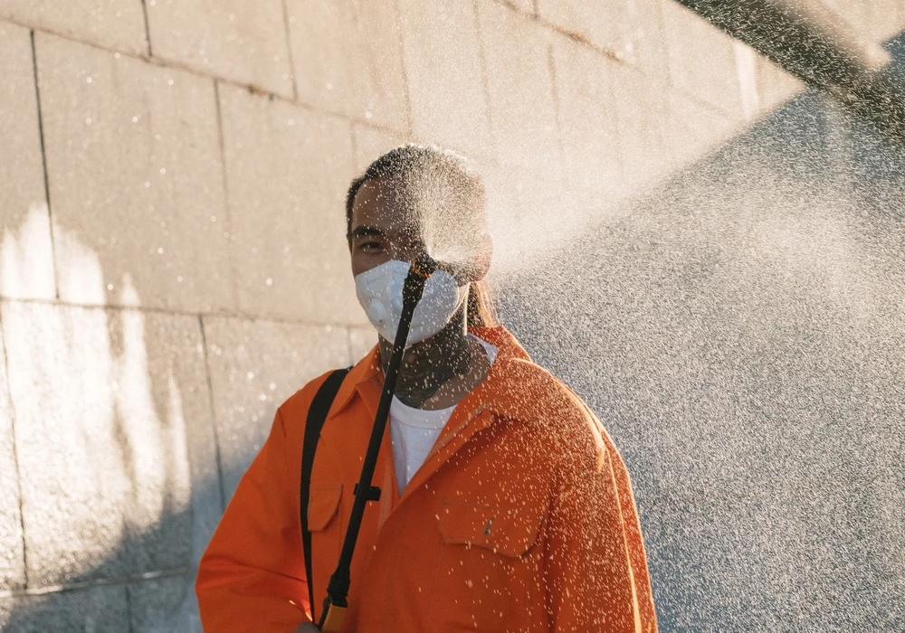 A masked worker sprays water across an exterior stone wall