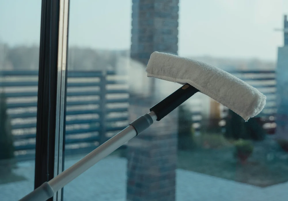 A long-handled window-washing applicator touches a glass pane