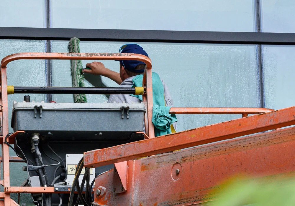 A window cleaner works from an elevated lift beside a glass building
