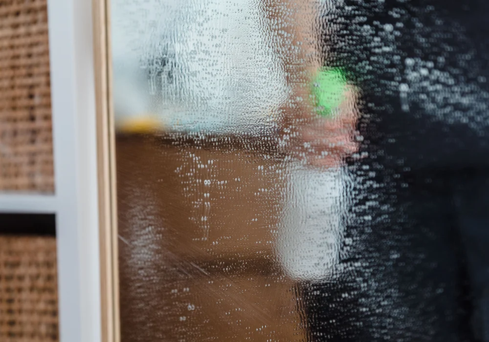 Water droplets cover a glass pane beside a window frame