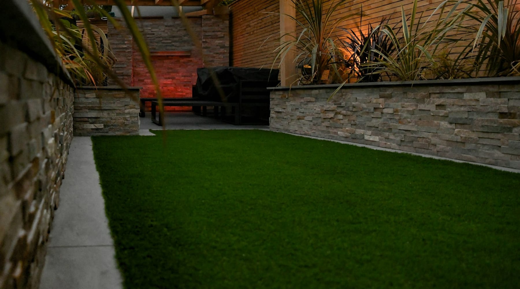 Lawn, stone planter walls and uplit planting in a landscaped courtyard at dusk