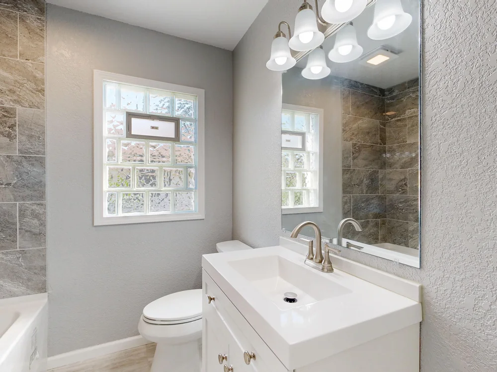 Bright bathroom with a white vanity, mirror and bathtub.