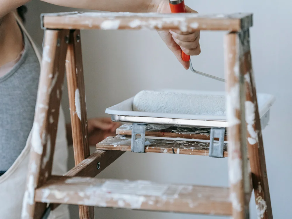 Paint roller and tray on a paint-splattered stepladder.