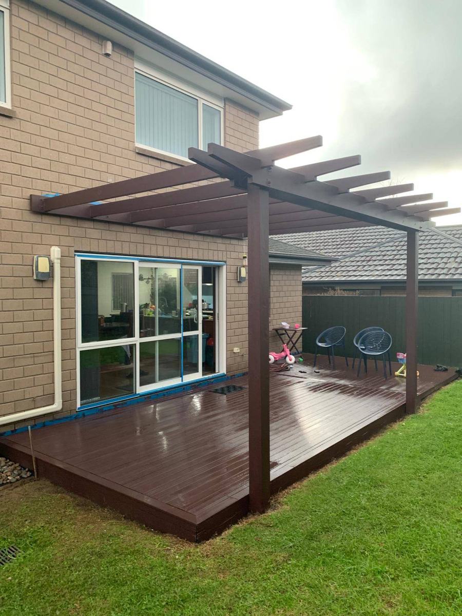 Timber deck and pergola beside a brick house with a lawn.