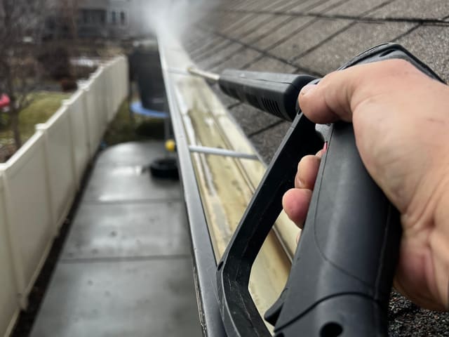 A gutter being cleaned by hand at roof height with a pressure washer.