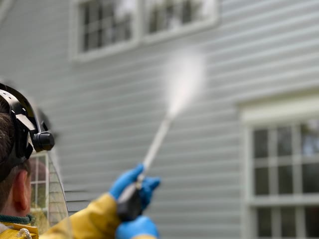 A pressure-washing wand spraying water across exterior wall cladding.