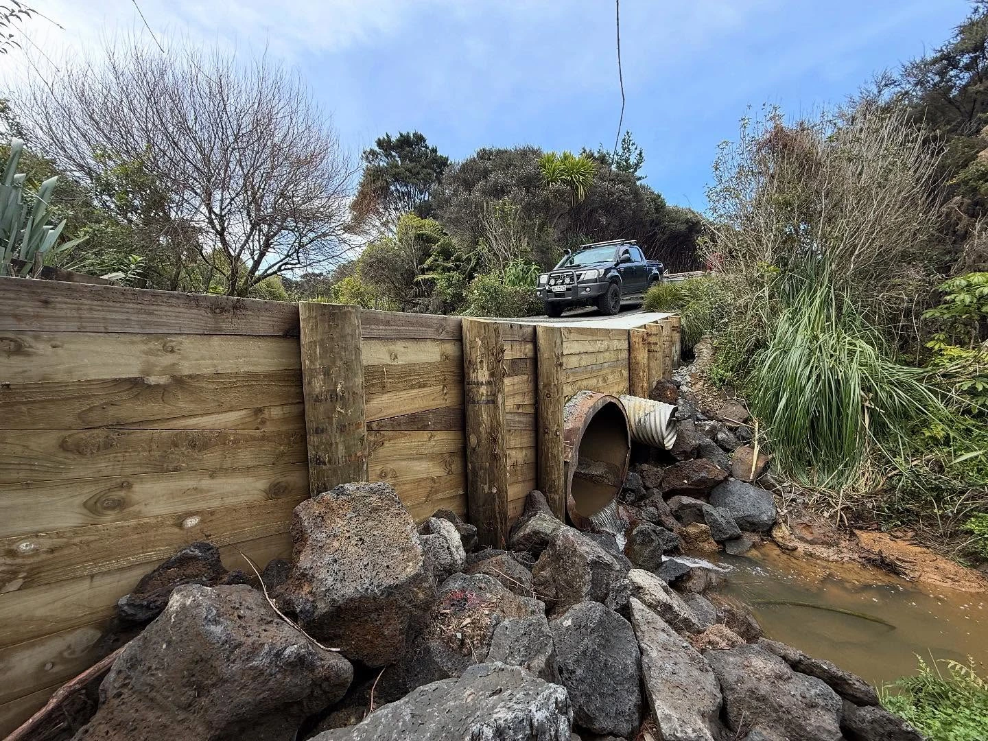 Timber retaining wall around a culvert beside a rocky stream