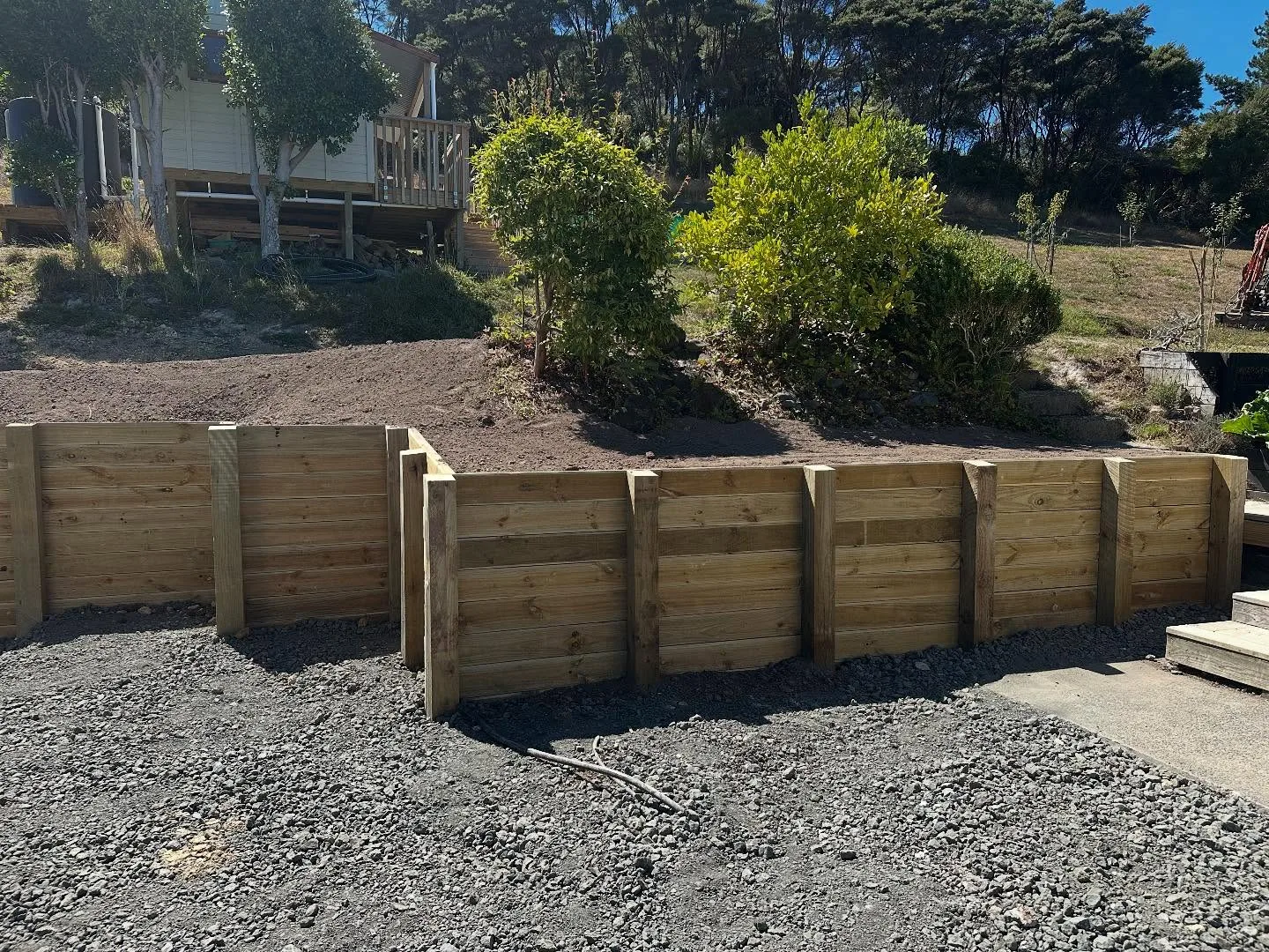 Timber post retaining wall with gravel backfill beside a garage slab